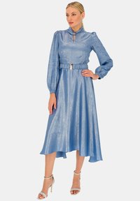 Jasnoniebieska sukienka o błyszczącej fakturze, z wysokim dekoltem, długimi bufiastymi rękawami oraz dopasowanym wcięciem w talii z paskiem. Spódnica opada do długości kolan.