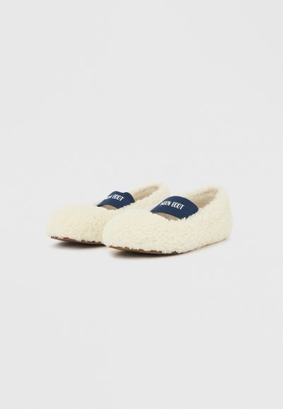 Paire de chaussons duveteux couleur crème avec des bandes élastiques bleu marine portant l'inscription "MOON BOOT" sur un fond blanc uni.