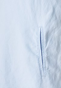 Ljusblå skjorta med en detaljerad bröstficka med en smal öppning, tillverkad av ett mjukt material med en slät yta.