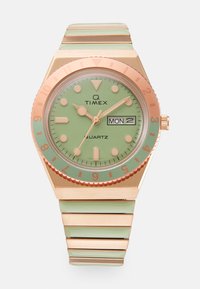 Montre quartz Timex Q avec un cadran vert menthe, un bezel en or rose et un bracelet en métal assorti. Dispose d'un affichage de la date et de grands index horaires.