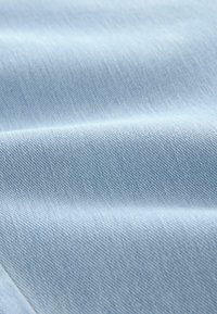Tela de mezclilla azul claro con una textura suave, que presenta un sutil patrón de tejido y pliegues suaves que indican suavidad y flexibilidad.