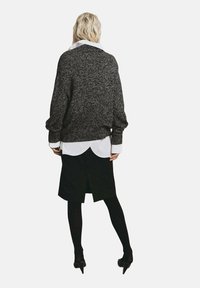 Maglioncino in maglia nero e grigio oversize indossato sopra una camicia bianca con colletto, abbinato a una gonna nera e a delle calze nere.