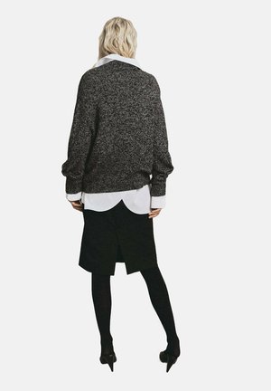 Suéter de punto negro y gris de gran tamaño superpuesto a una camisa blanca con cuello, combinado con una falda negra y medias negras.