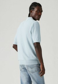 Valaistuksella sininen lyhythihainen polo-paita teksturoidusta neuloksesta, yhdistettynä vaaleansinihin farkkuihin. Rennon mallinen, jossa ribbireunukset hihoissa ja helmassa.