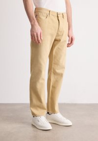 Jeans din bumbac khaki cu o croială dreaptă, cinci buzunare și închidere cu nasture. Asortați cu adidași albi. Textură netedă, design clasic.