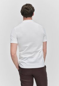 Vit kortärmad t-shirt i en mjuk bomullsblandning, med en enkel design och rund halsringning. Bärs med mörkbruna byxor.