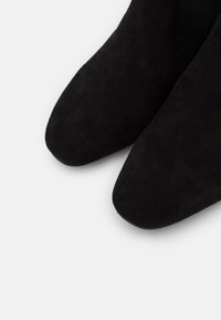 Botines de ante negro con punta afilada, que presentan una textura suave y un diseño elegante, enfatizando una estética minimalista.