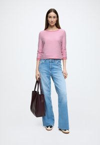 Roze gestreept top met lange mouwen, lichtblauwe jeans met brede pijpen en een donker bordeauxrode shopper. Sneakers met patroonaccenten op de voeten.