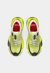 Ζευγάρι αθλητικών παπουτσιών Camper σε νεον κίτρινο, μπεζ και μαύρο χρώμα με χοντρές σόλες και κόκκινες σόλες εσωτερικά, απεικονίζεται από πάνω σε λευκό φόντο.