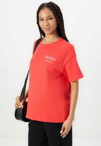 Camiseta de algodón roja con mangas cortas y cuello redondo, con texto bordado en blanco que dice "MAMA" y "significa todo para ti" en la parte frontal.