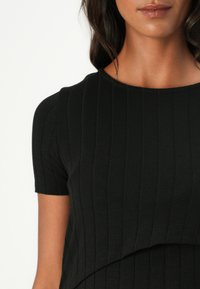 Μαύρη ριμπ μπλούζα κοντό μανίκι με στρογγυλή λαιμόκοψη, διαθέτοντας υφή και μαλακό ύφασμα, τονίζοντας τον επικείμενο λεπτό σχεδιασμό.