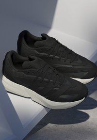 Čierne športové topánky s textúrovaným sieťovinovým zvrškom, štýlovým dizajnom a kontrastnou bielou podrážkou. Medzi funkcie patrí šnurovanie a detailovanie značky na boku.