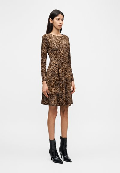 Φόρεμα με λεοπάρ τύπωμα και μακριά μανίκια, με σφηκοφωλιά στη μέση, φουσκωτή φούστα και πλαϊνές τσέπες. Συνδυασμένο με γυαλιστερά μαύρα μποτάκια αστραγάλου.