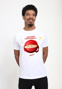 Bílé tričko s červenou karikaturou sýrového kolečka s usmívající se tváří a textem "MŮŽE TO ZNÍT SÝROVĚ...", značky "Babybel."