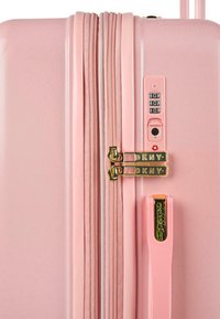 Maleta dura rosa con superficie texturizada, dos cremalleras doradas, candado de combinación y asa rosa a juego.