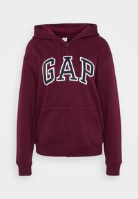 Sudadera con cremallera en burdeos con el logotipo blanco de "GAP". Cuenta con capucha con cordones, dos bolsillos frontales y puños y dobladillo de canalé. Textura de tela suave.
