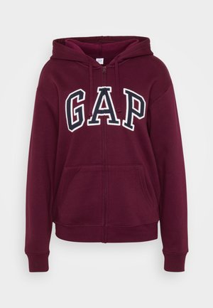 Burgundska zip-up kapuca s belim "GAP" logotipom. Ima kapuljaču s vezicom, dva prednja džepa i rebraste rukave i donji deo. Mekana tekstura tkanine.