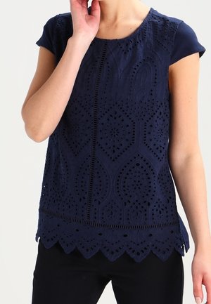 Navyblauw top met korte mouwen, voorzien van ingewikkelde uitsnijdingen en een golvende zoom. Gemaakt van een lichtgewicht stof met een textuurafwerking.