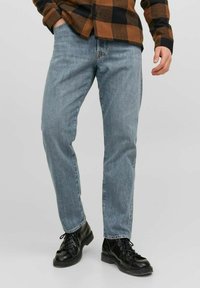 Jeans de mezclilla azul claro con corte recto, que presentan un diseño clásico de cinco bolsillos y sutiles detalles de decoloración. Llevados con botas negras con cordones.