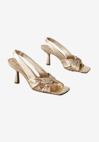 Złote metaliczne szpilki slingback z kwadratowym noskiem, zawiązanym przodem i smukłym, cylindrycznym obcasem. Gładka tekstura z połyskującym wykończeniem.