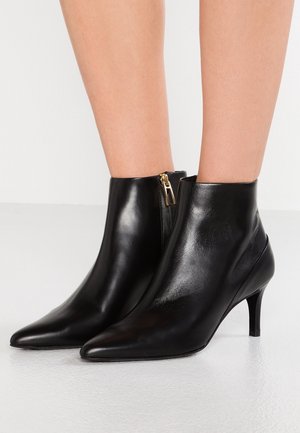 Bottes cheville en cuir noir avec un bout pointu et un petit talon. Dotées d'une fermeture éclair latérale et d'une texture lisse.