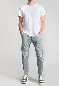 Biała bawełniana koszulka zestawiona z jasnoszarymi dżinsami o dopasowanym kroju. Model nosi czarno-białe sneakersy.