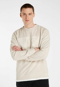 Licht beige sweatshirt met een gestructureerd horizontaal paneel met het "NXG"-logo in het midden. Geribbelde manchetten en ronde halslijn.