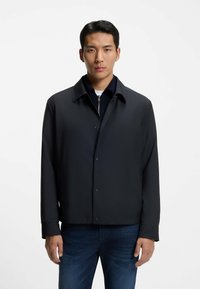 Dark blue jacket featuring a collared neckline, snap front closure, and long sleeves. Smooth fabric with a structured, modern fit.