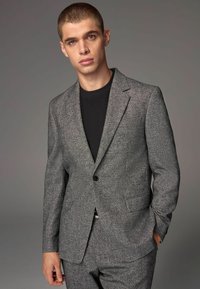Grå tekstureret jakkesætjakke med notched lapels, enkelt knaplukning og sidelommer, parret med en sort skjorte.