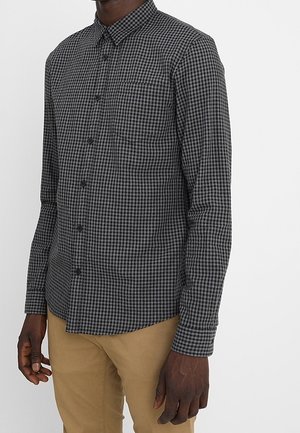 Camicia a maniche lunghe a scacchi neri e grigi con colletto a button-down, tasca sul petto singola e design aderente. La trama del tessuto appare liscia.