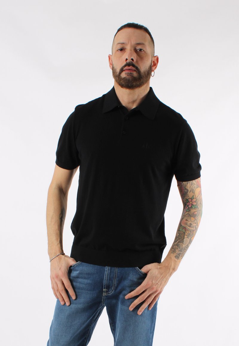 Svart kortärmad polo skjorta med nedfälld krage och tre knappar. Mjuk textur och figursydd design. Bärs med blå jeans.