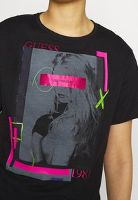 Zwarte t-shirt met een grafische print in grijswaarden met roze en groene accenten, inclusief de tekst "LOST IN LUST" en "1981".