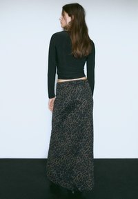 Maglietta nera a maniche lunghe e una gonna fluida lunga fino alla caviglia con un motivo a macchie di leopardo scuro, realizzata in materiale leggero.