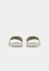 Lys grå slidesandaler med åpen bak, robuste såler og glatt tekstur, med et enkelt design og minimal detaljering.