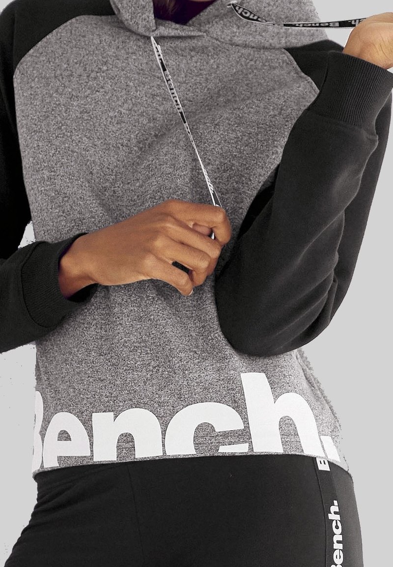 Sweat à capuche gris et noir en tissu texturé, avec un logo à la taille, des manches contrastées et des cordons de serrage avec détails de la marque.