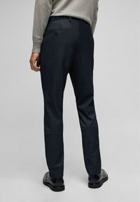 Donkerblauwe op maat gemaakte broek van een gestructureerde stof, met een enkele achterzak met knoopsluiting, aangevuld met slanke zwarte schoenen.