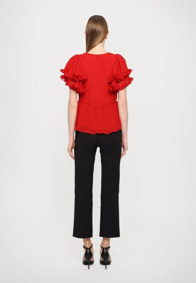 Red peplum top with textured fabric, short ruffled sleeves, and a scalloped hem, paired with black fitted pants and black heels.