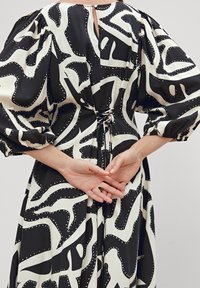 Robe à motifs noir et blanc avec des manches bouffantes, une taille à nouer et une fermeture à boutons au dos, ornée de accents en points tout au long.