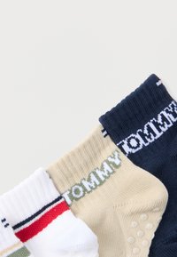 Trois paires de chaussettes côtelées pliées en blanc, beige et marine, chacune avec le logo "TOMMY" et des semelles antidérapantes sur les chaussettes beiges.