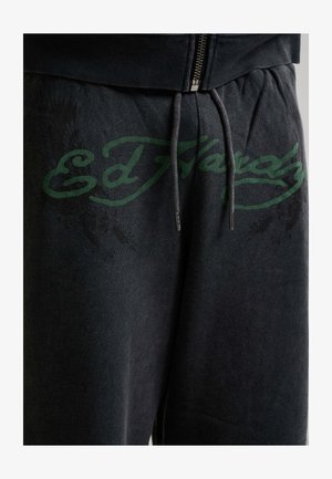 Donkergrijze sweatpants met een groen "Ed Hardy" logo over de voorkant van de taille, voorzien van een trekkoord en ritssluiting aan het bovenstuk.