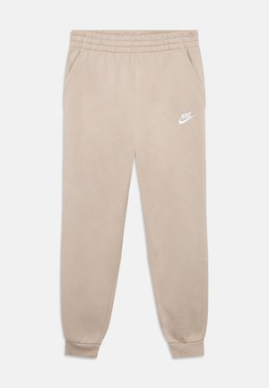 Bēšas Nike sporta bikses ar elastīgu jostasvietu, sānu kabatām, manžetēm pie potītēm un baltu Nike logo uz kreisās augšstilba puses.