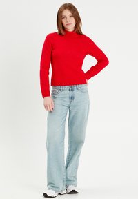 Pull en maille rouge à col roulé avec ourlet côtelé, associé à un jean large bleu clair. Un style décontracté présentant une coupe ample.