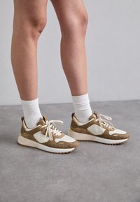 Brune og kremfargede sneakers med teksturert design, med hvite snørebånd, polstret krage og gummisåle med en subtil logo-detalj.