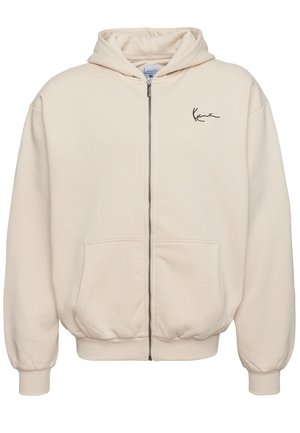 Beige rits-hals trui van zachte stof. Heeft een voorzichtingsrits, twee zakken en een geborduurd logo op de linkerborst.