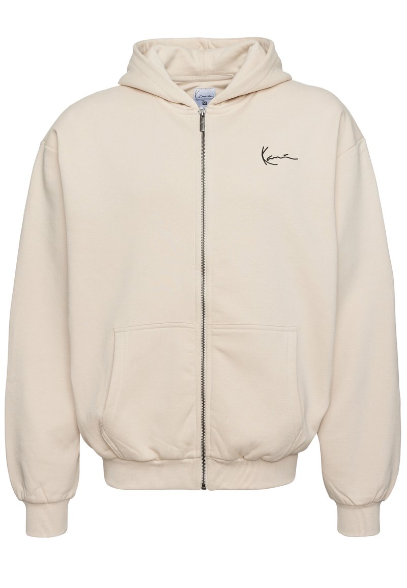 Beige rits-hals trui van zachte stof. Heeft een voorzichtingsrits, twee zakken en een geborduurd logo op de linkerborst.