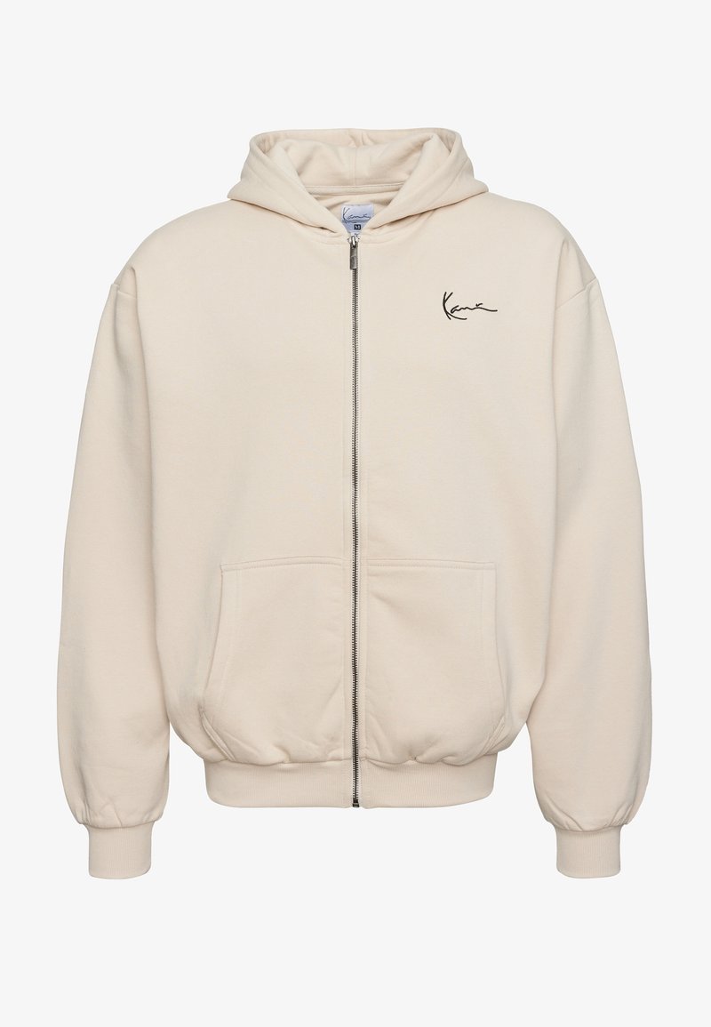 Beige rits-hals trui van zachte stof. Heeft een voorzichtingsrits, twee zakken en een geborduurd logo op de linkerborst.