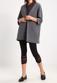 Grå texturerad cardigan med öppen framsida, parat med svarta leggings med spetsdetaljer vid fållen, och blanka svarta loafers.