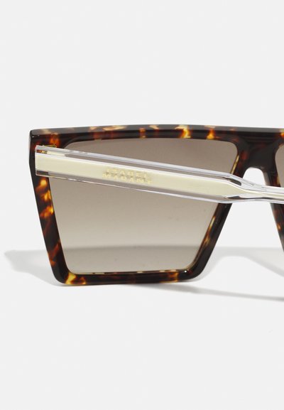 Schildpadbril met rechthoekige lenzen, donkere gradienttint, heldere pootjes, en een gouden accent met de merknaam.