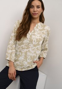 Helebeež blouse valge lillemustriga, mis on varustatud V-kaelusega, kolmandiku pikkusega varrukatega ja lõdva lõikega. Kombineeritud tumedate pükstega.