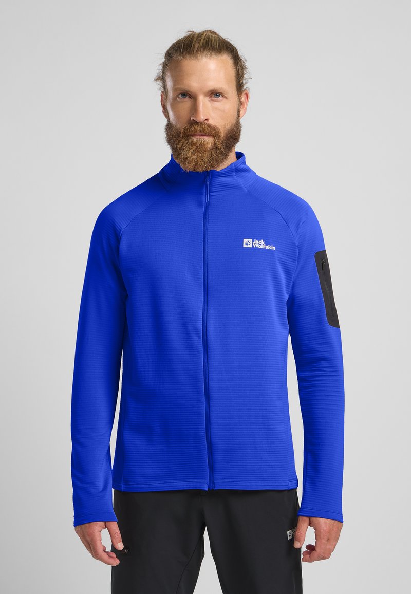 Blaue Reißverschlussjacke aus strukturiertem Stoff, mit langen Ärmeln und einem schwarzen Akzent am linken Arm. Verfügt über ein Logo auf der Brust.